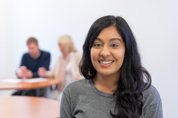 Woman smiling in business training room with two people discussing in background