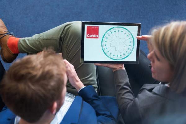 Businesswoman sitting next to businessman showing tablet displaying Cubiks personality assessment report